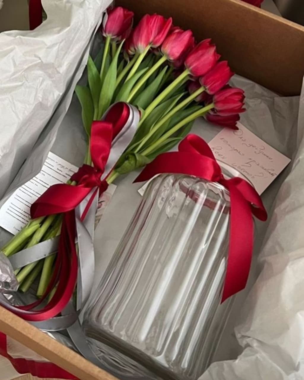 Bouquet of red tulips with a glass vase and red ribbon inside a box.
